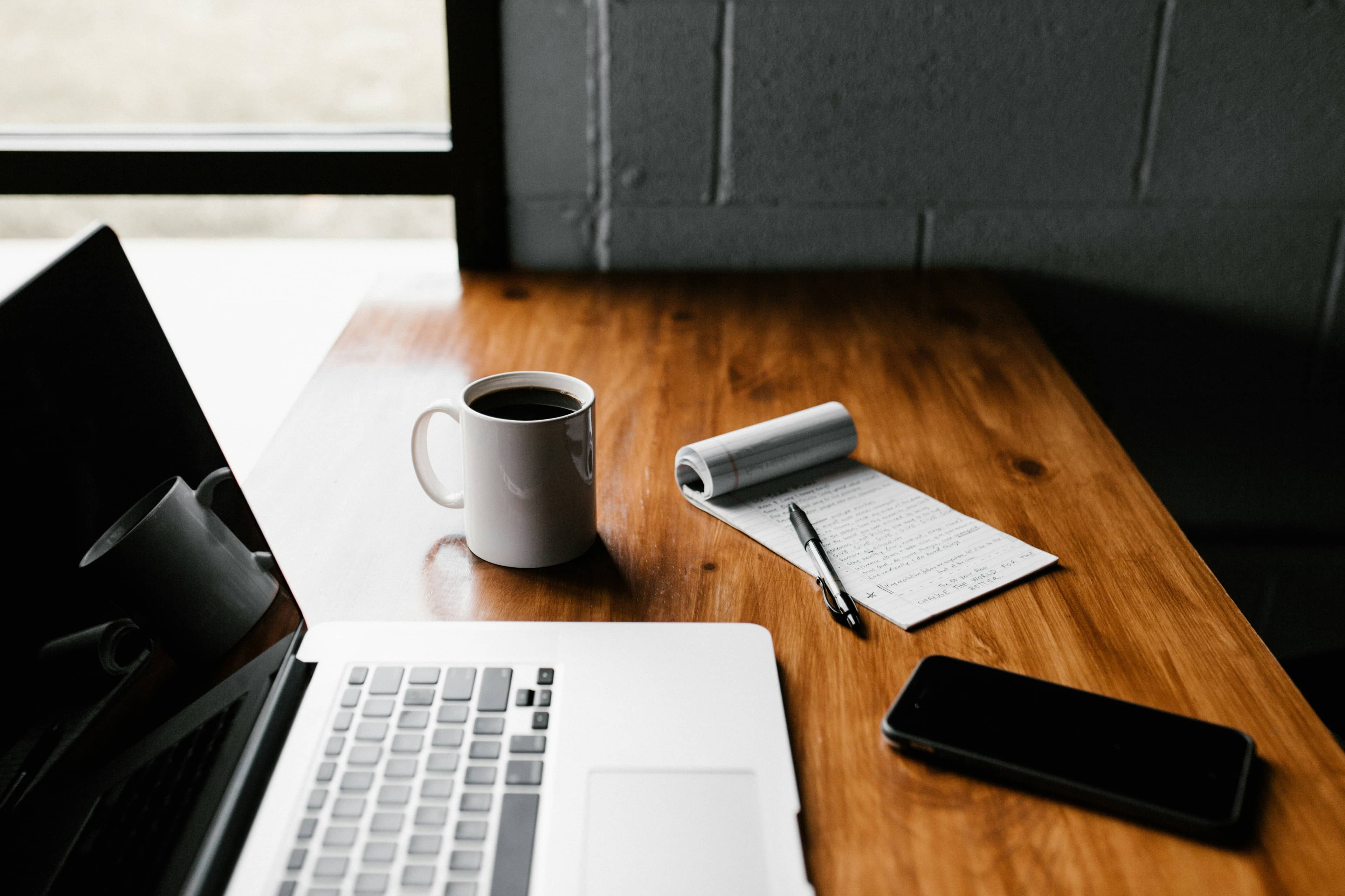 A laptop, notebook and coffee on a wooden desk